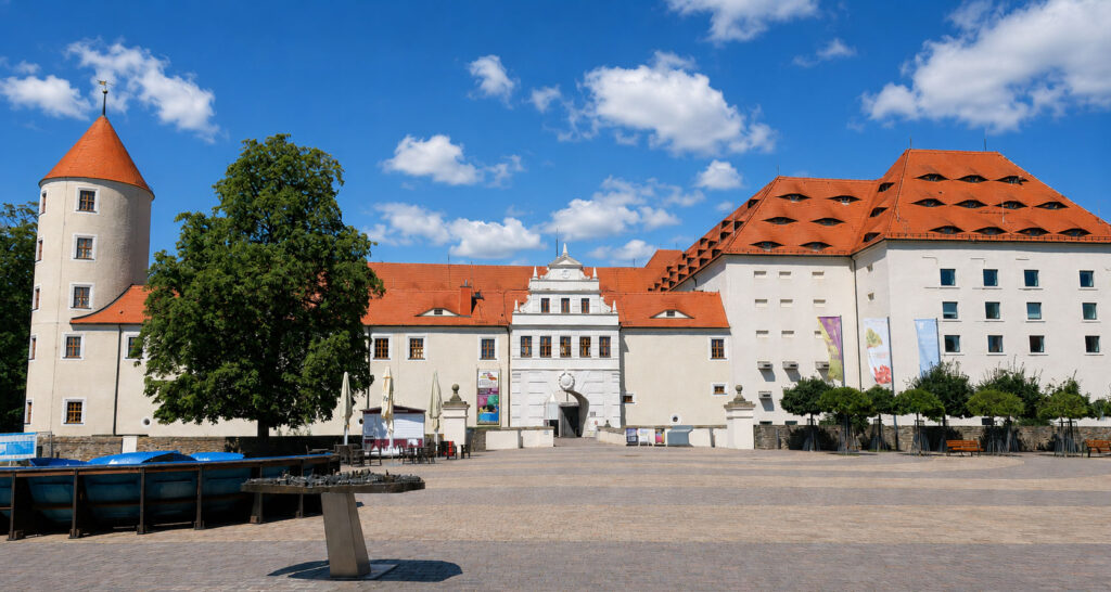 Schloss Freudenstein mit großem Baum und Tastmodell auf dem Vorplatz bei blauem Himmel mit vereinzelten Wolken.