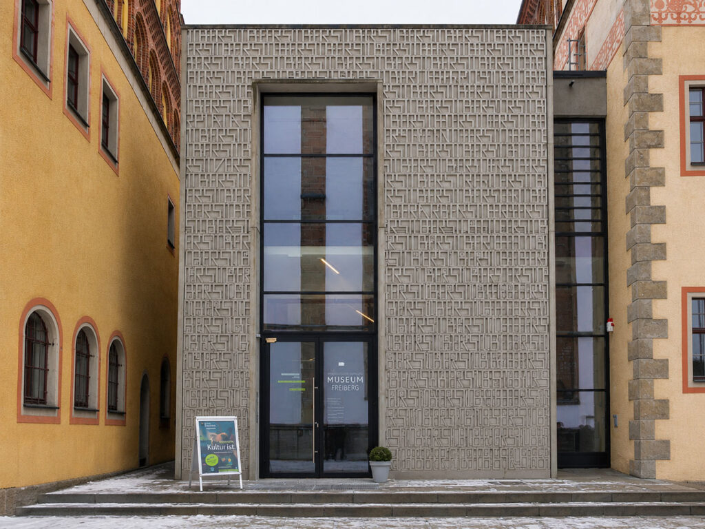 Eingang eines Stadt- und Bergbaumuseums mit moderner Fassade aus rechteckigen Mustern zwischen zwei älteren Gebäuden.