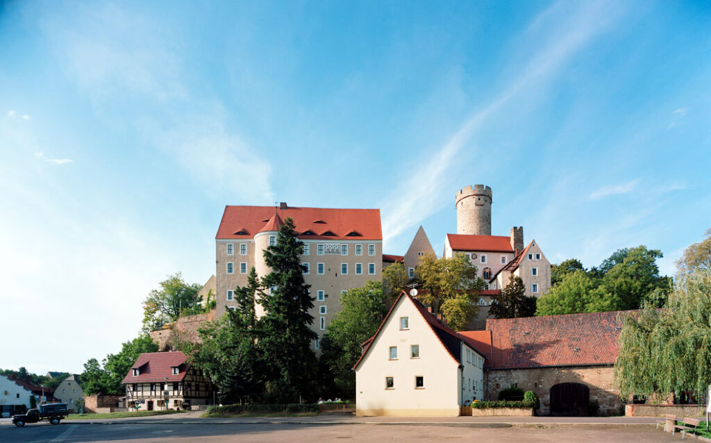 Burg Gnandstein auf einem Hügel mit mehreren Gebäuden und einem runden Turm bei klarem Himmel
