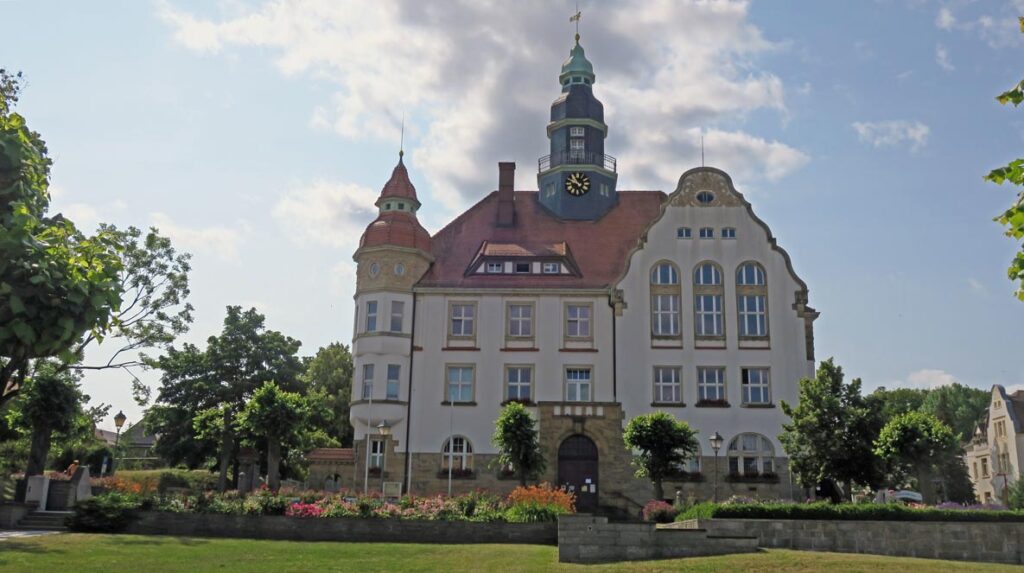 Historisches mehrstöckiges Gebäude mit Turm und Uhr, umgeben von Garten und Bäumen