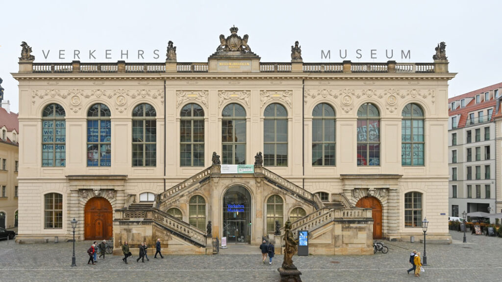 Frontansicht des Verkehrsmuseums Dresden mit klassizistischer Fassade, zwei symmetrischen Außentreppen und Schriftzug 'VERKEHRS MUSEUM' auf dem Dach.